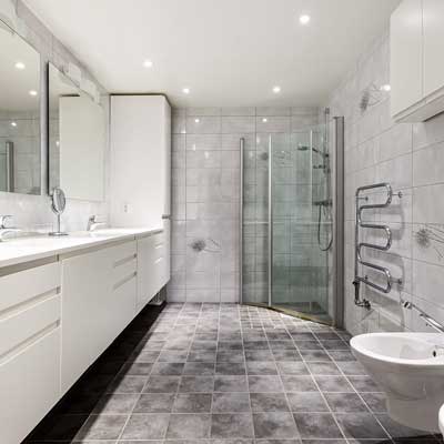 bathroom-installations-by-grimsby-plastering-services A bathroom showing white cabinets, a corner shower, towel rail bidet and grey tiled walls with a grey lino floor
