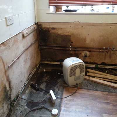 repairs-to-damp-walls-with-Grimsby-Plastering-Services An image of a damp corner of a kitchen showing damp walls pipes and a dehumidifier