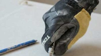 A plasterer wearing a glove cutting plasterboard with a knife and ruler